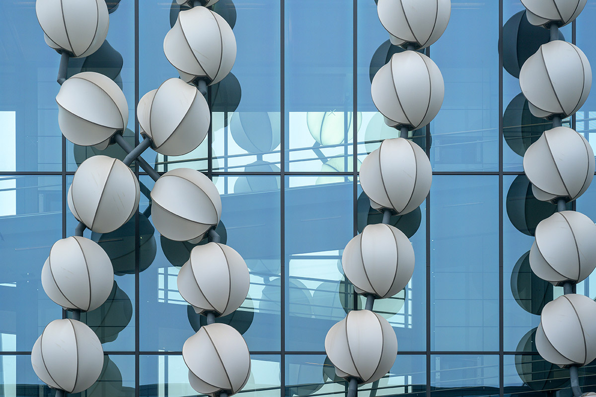 Artwork Gadget: Close-up of a glass facade with reflective, white spherical sculptures arranged vertically.