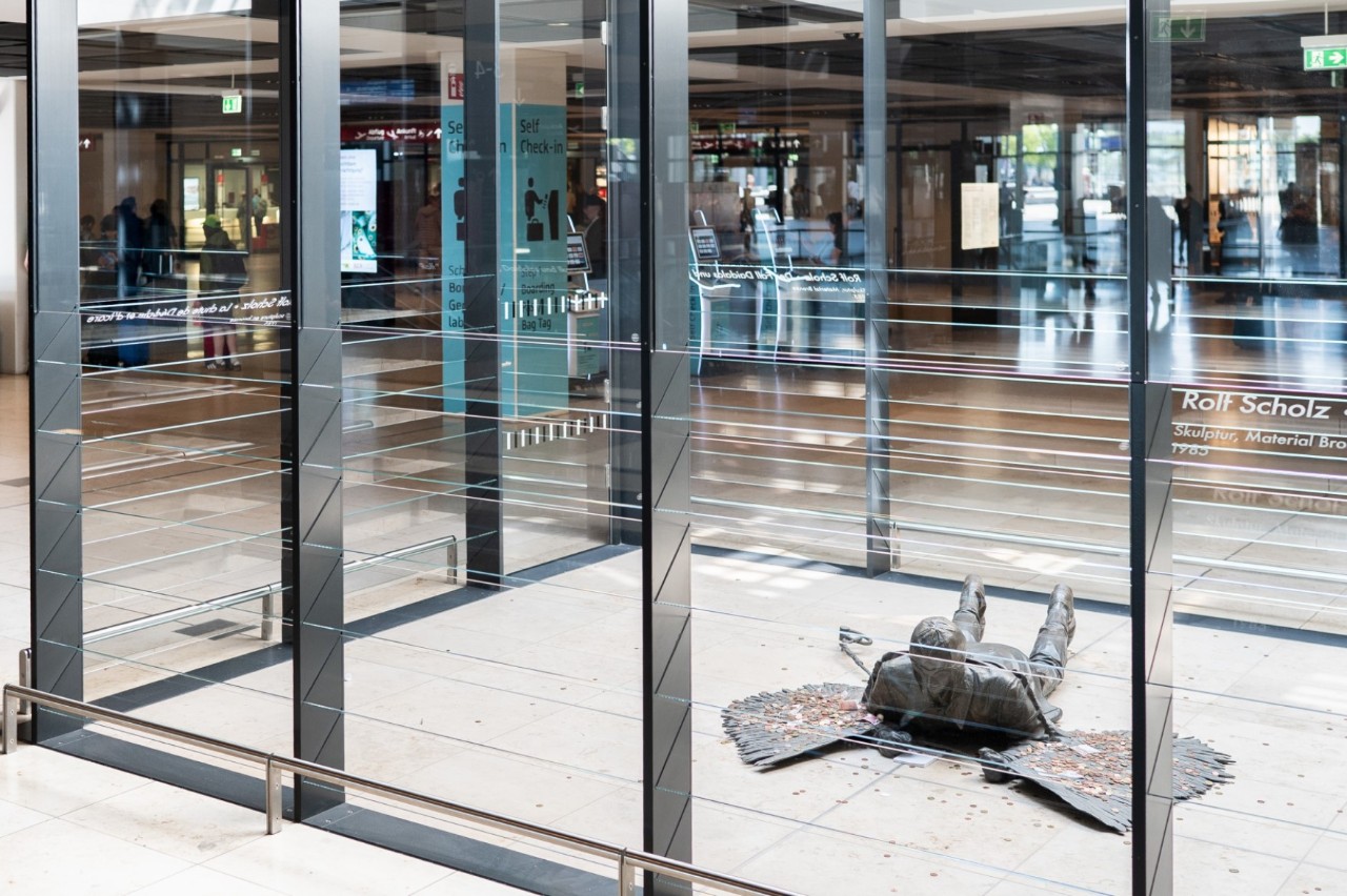 Bronze sculpture by Rolf Scholz (1985) in the entrance area of Terminal 1 at BER. It depicts a pilot wearing a leather cap and wings lying on the ground—an homage to Otto Lilienthal and the Greek myth of Daedalus and Icarus.