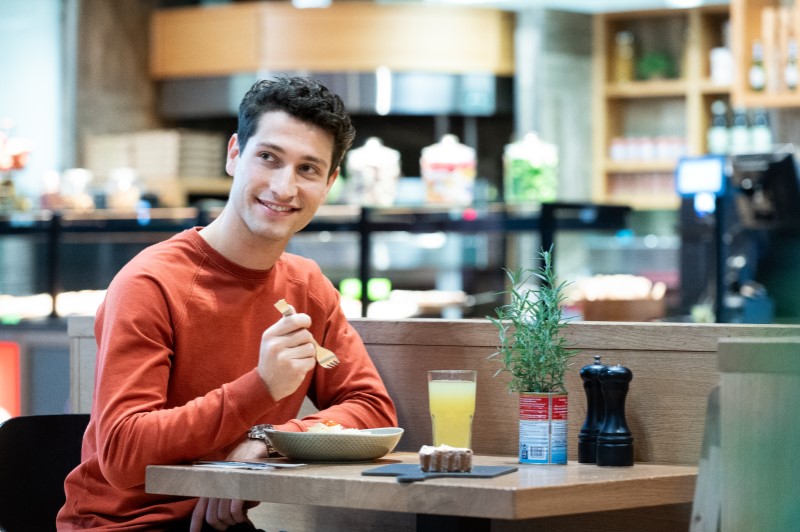 Man sitting in a bisto eating a meal. A glass of orange juice is on the table.