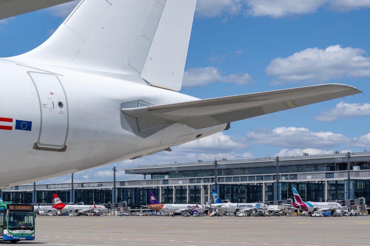 Im Vordergrund ein weißes Tail eines Flugzeuges. Im HIntergrund das Terminal 1 mit Flugzeugen davor.