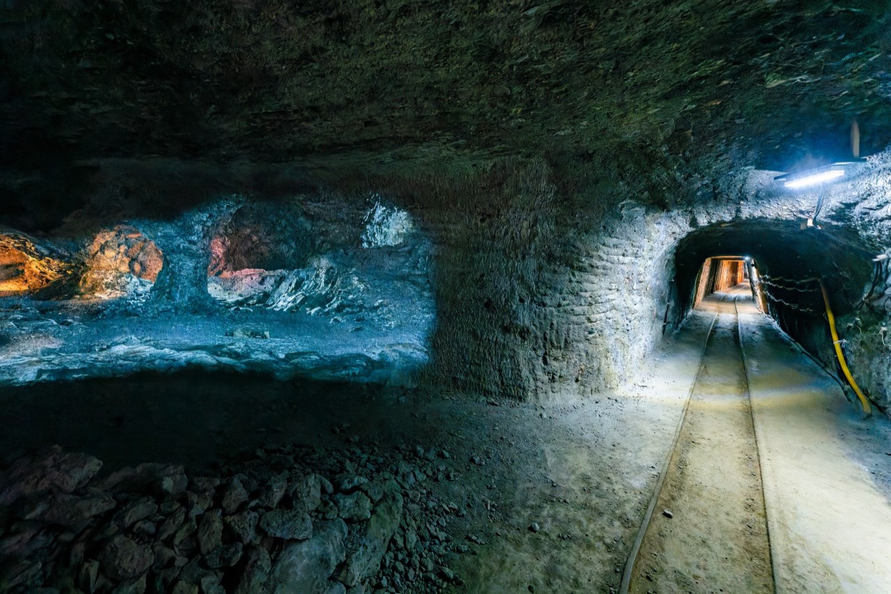 The inside of a mine with a blue illuminated cavity on the left. On the right of the picture is a tunnel with a track bed, also illuminated by a light source.