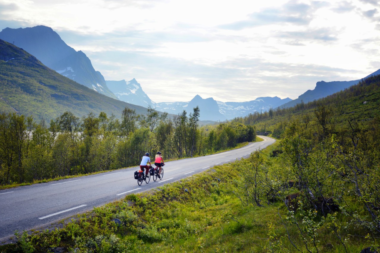 Cyclist on Norwegian country road with mountains in the background.