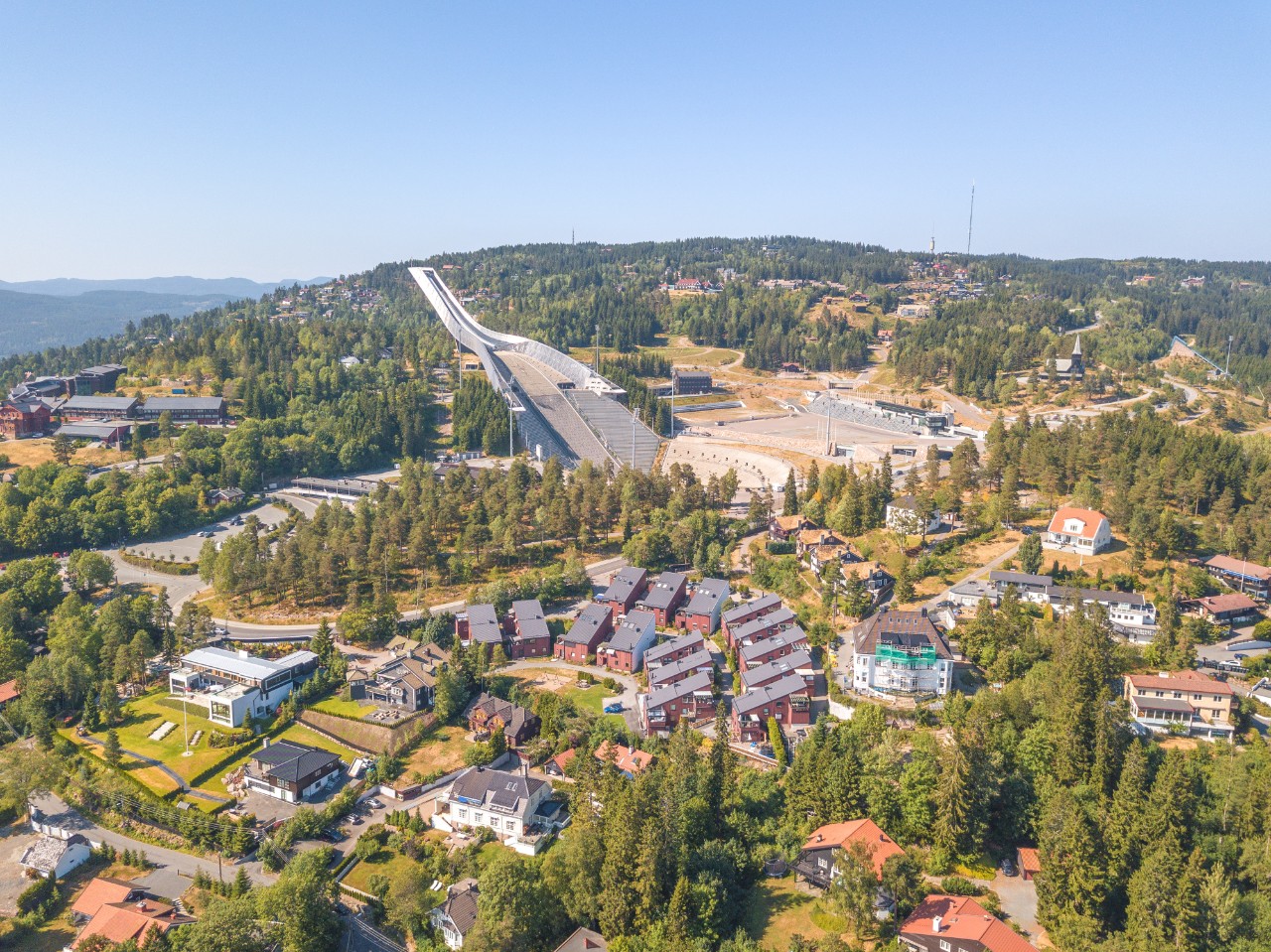 Holmenkollen ski jump in Oslo seen from afar with forested slope.