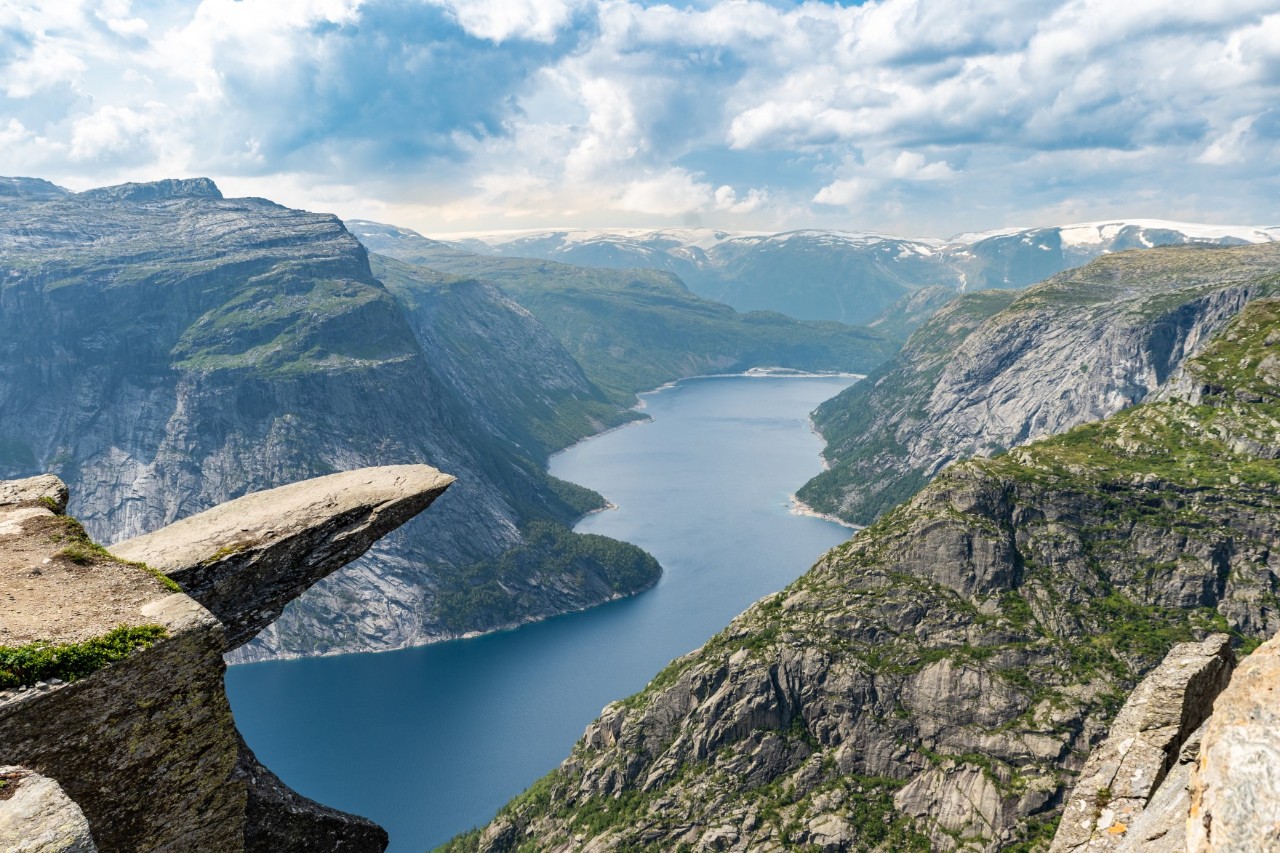 Trolltunga rock juts over deep valley with lake and mountains.