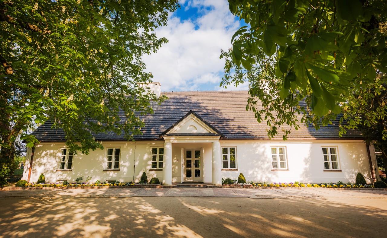 Chopin's white birthplace with garden and trees in summer.