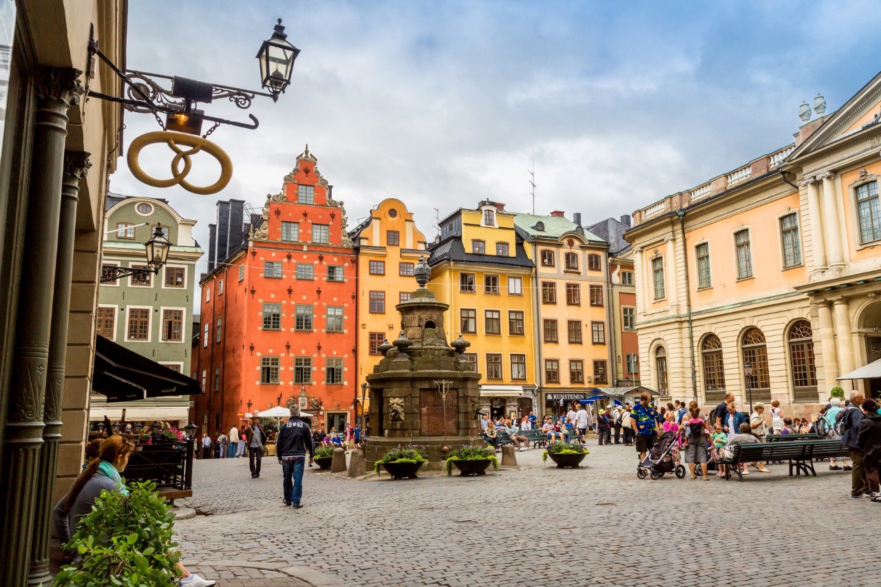 People at Stortorget square with fountain and colorful gabled buildings.