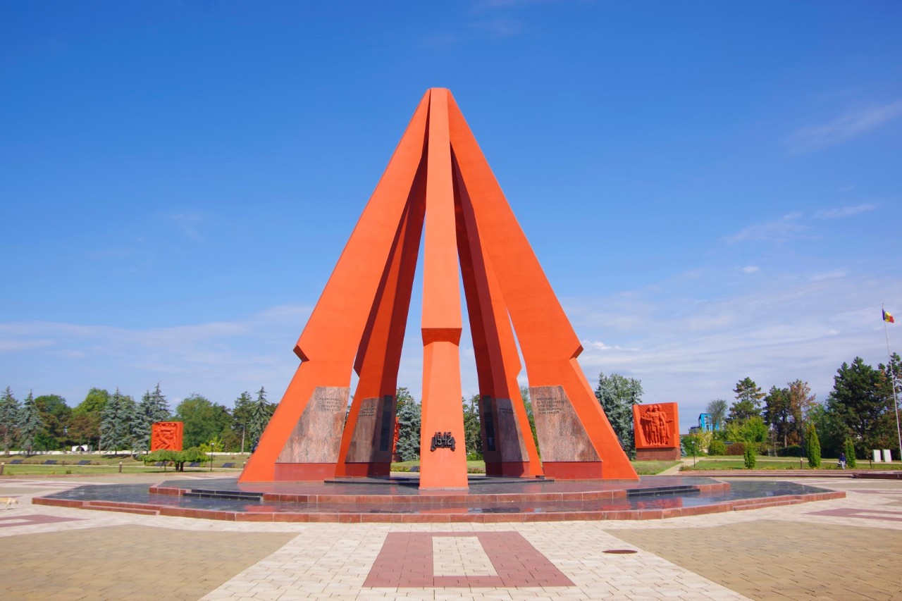 Red war memorial in the shape of a triangle, blue sky 