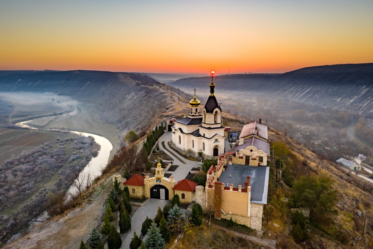 Orheiul Vechi Monastery on a mountain with courtyard and several buildings, limestone cliffs and river in the background, fog, sunrise © Calin Stan/stock.adobe.com