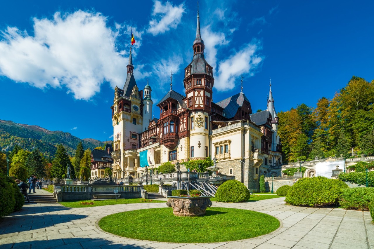 Red-and-white castle with turrets surrounded by greenery on a sunny day. 