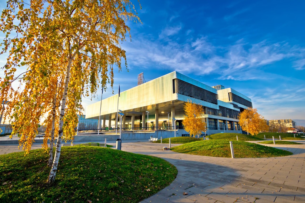 Modern building with green area, trees with autumn leaves and paths 