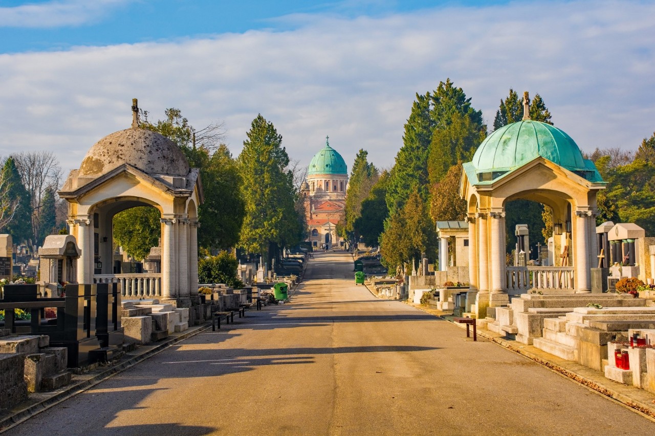 Wide path leading to a church, surrounded by graves, chapels and trees 