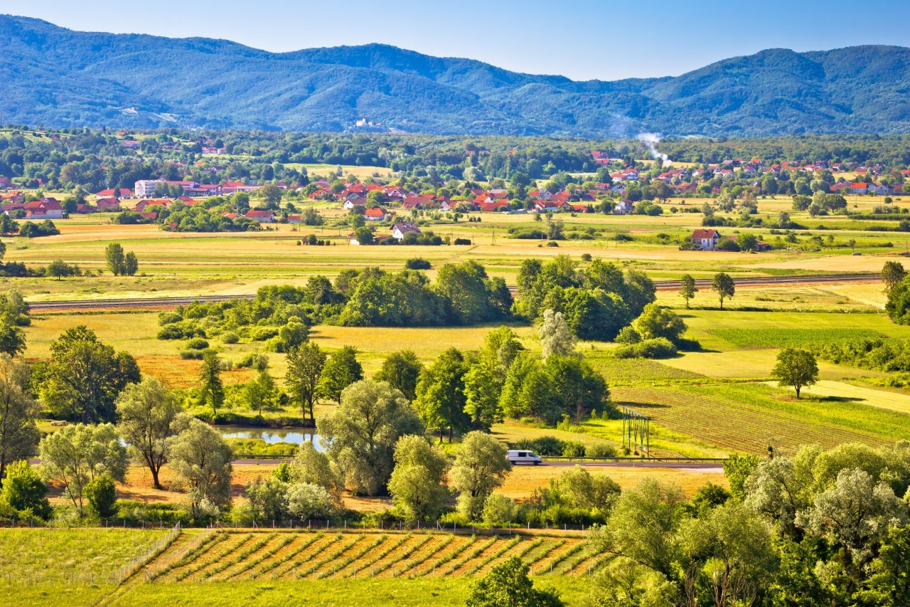 Green, expansive valley with meadows, trees, lake, villages and mountains in the background 