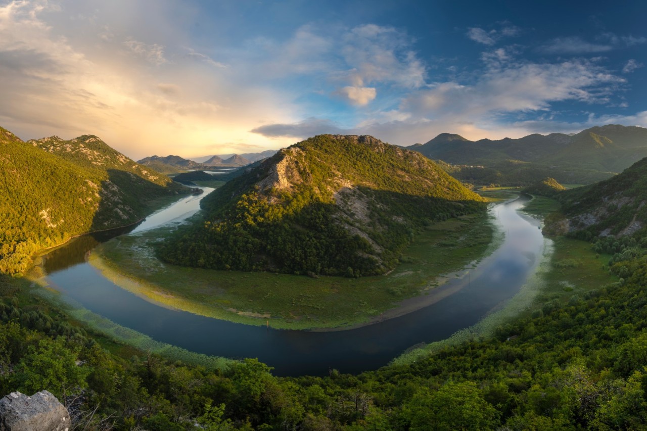 Aerial view of a river bend in the middle of a green hilly landscape, winding around a green hill.