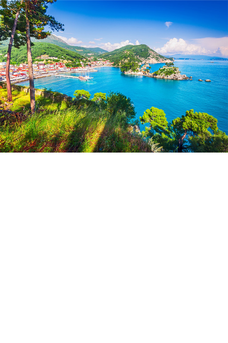 View from above of a coastal landscape with a small town by the sea. The houses have red roofs. The turquoise blue sea is surrounded by green hills and small islands.