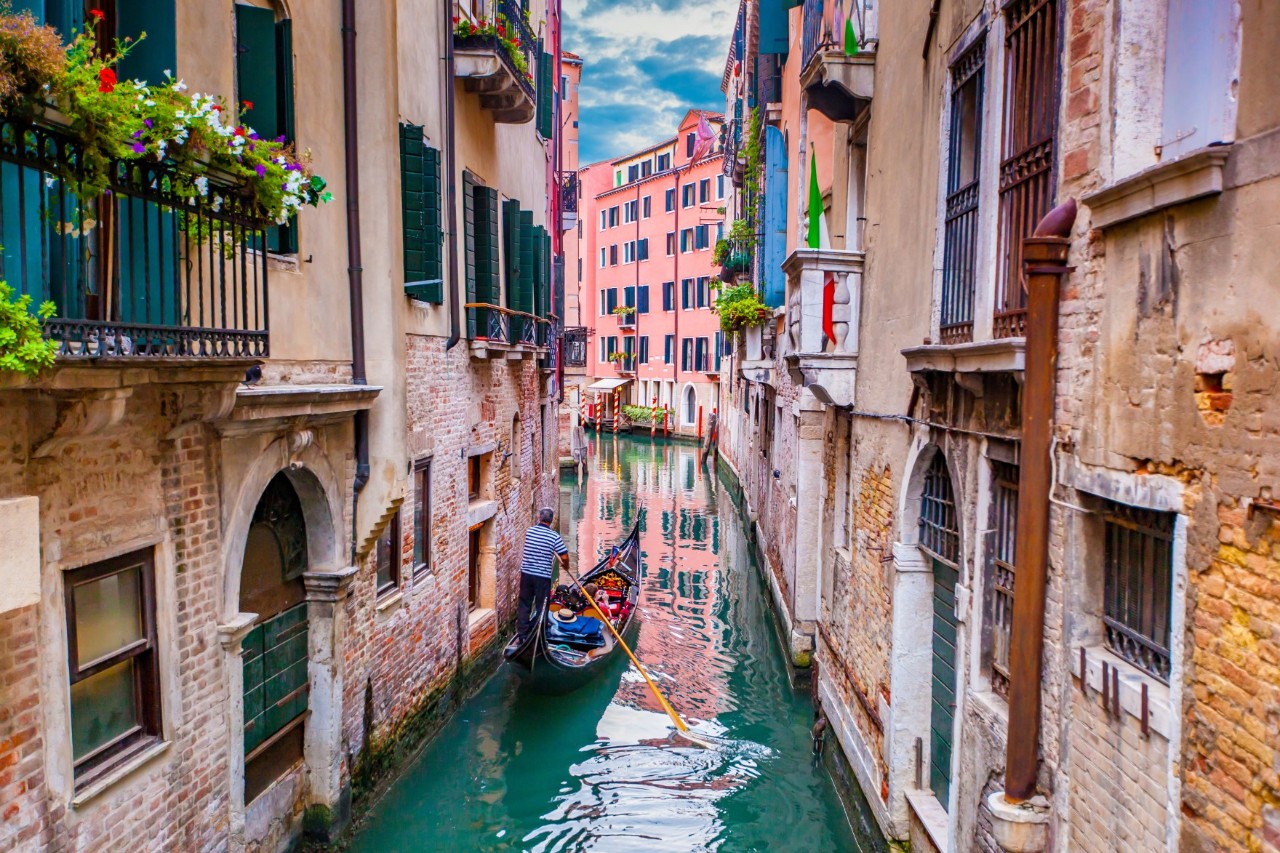 Narrow canal, gondola with tourists and gondoliers, typical Venetian old houses. © James Ser/stock.adobe.com