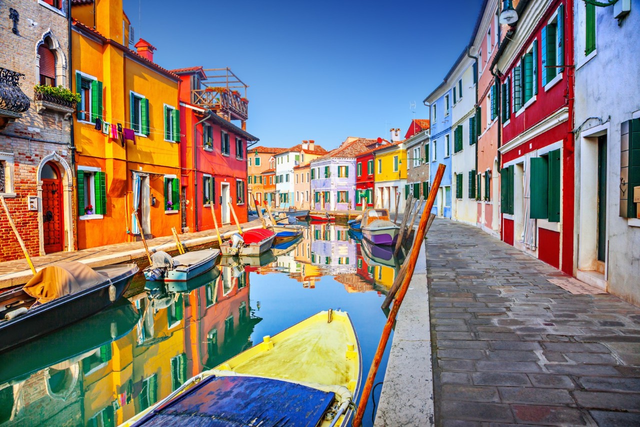 Burano island with colorful fishermen's houses, canal with boats, paved path. © adisa/stock.adobe.com 