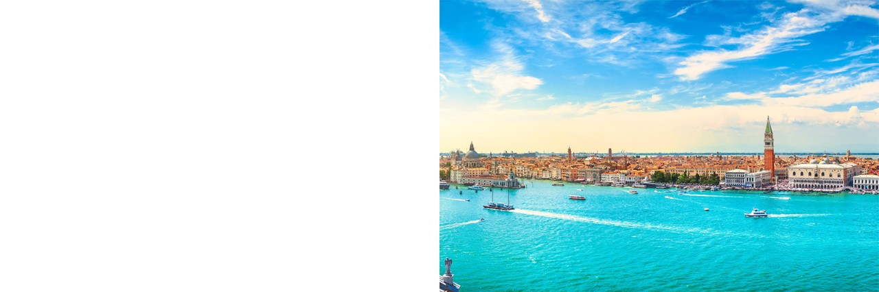 Aerial view of a city with turquoise-blue water and boats in the foreground and numerous buildings in the background. 