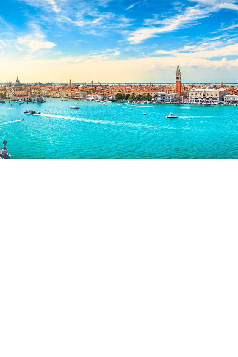 Aerial view of a city with turquoise-blue water and boats in the foreground and numerous buildings in the background. 