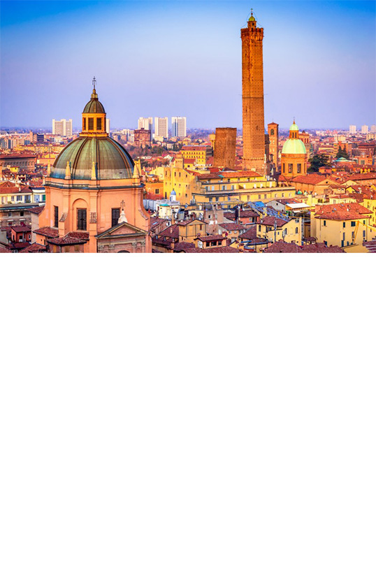 Aerial view of a large city in the reddish evening light. In the foreground is a large, round church dome behind which are numerous houses with tiled roofs and historic buildings as well as two adjacent square towers, one of which is significantly higher than the other.