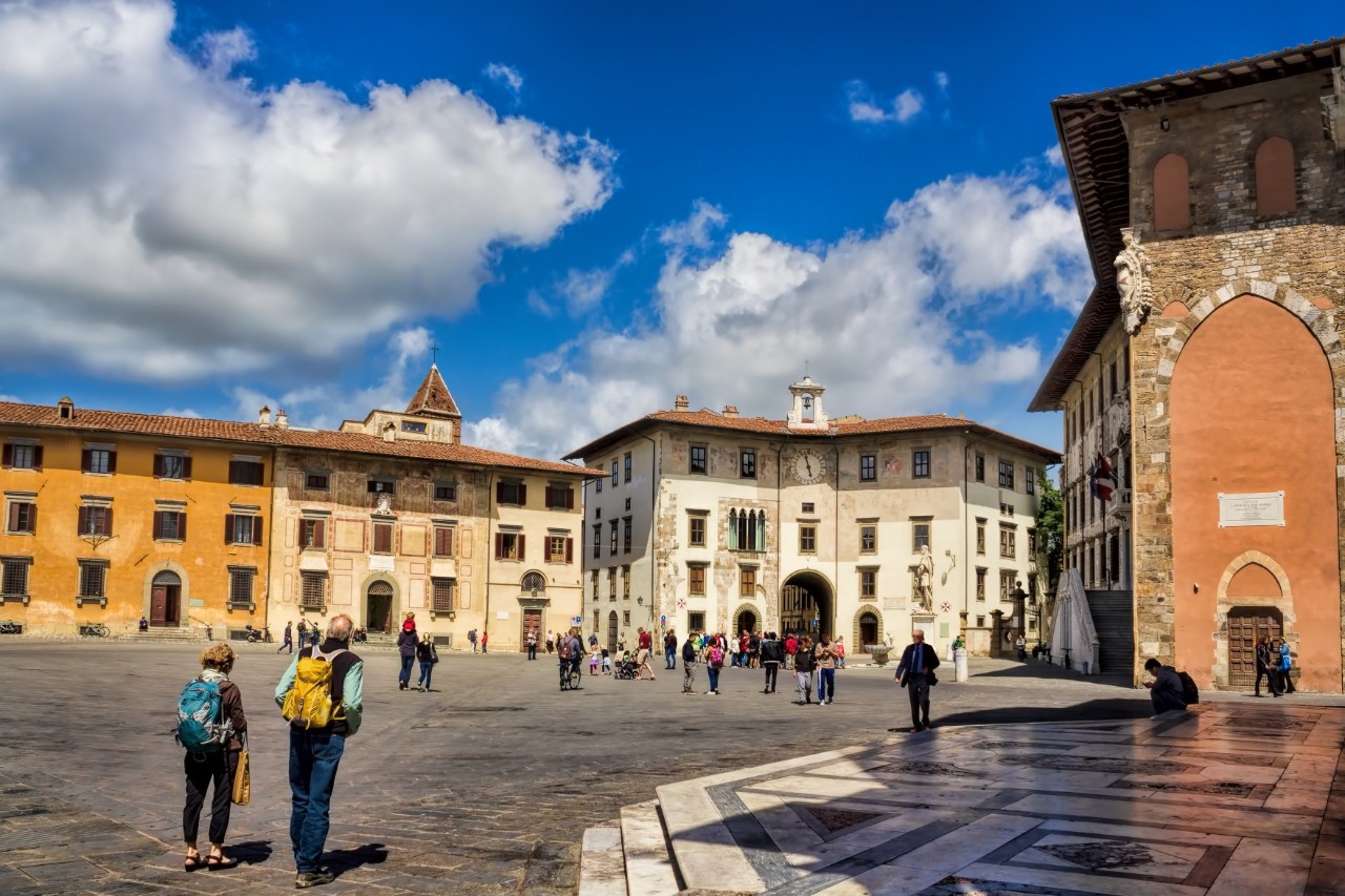 View of a large square surrounded by historic buildings. Several people can be seen on the square 