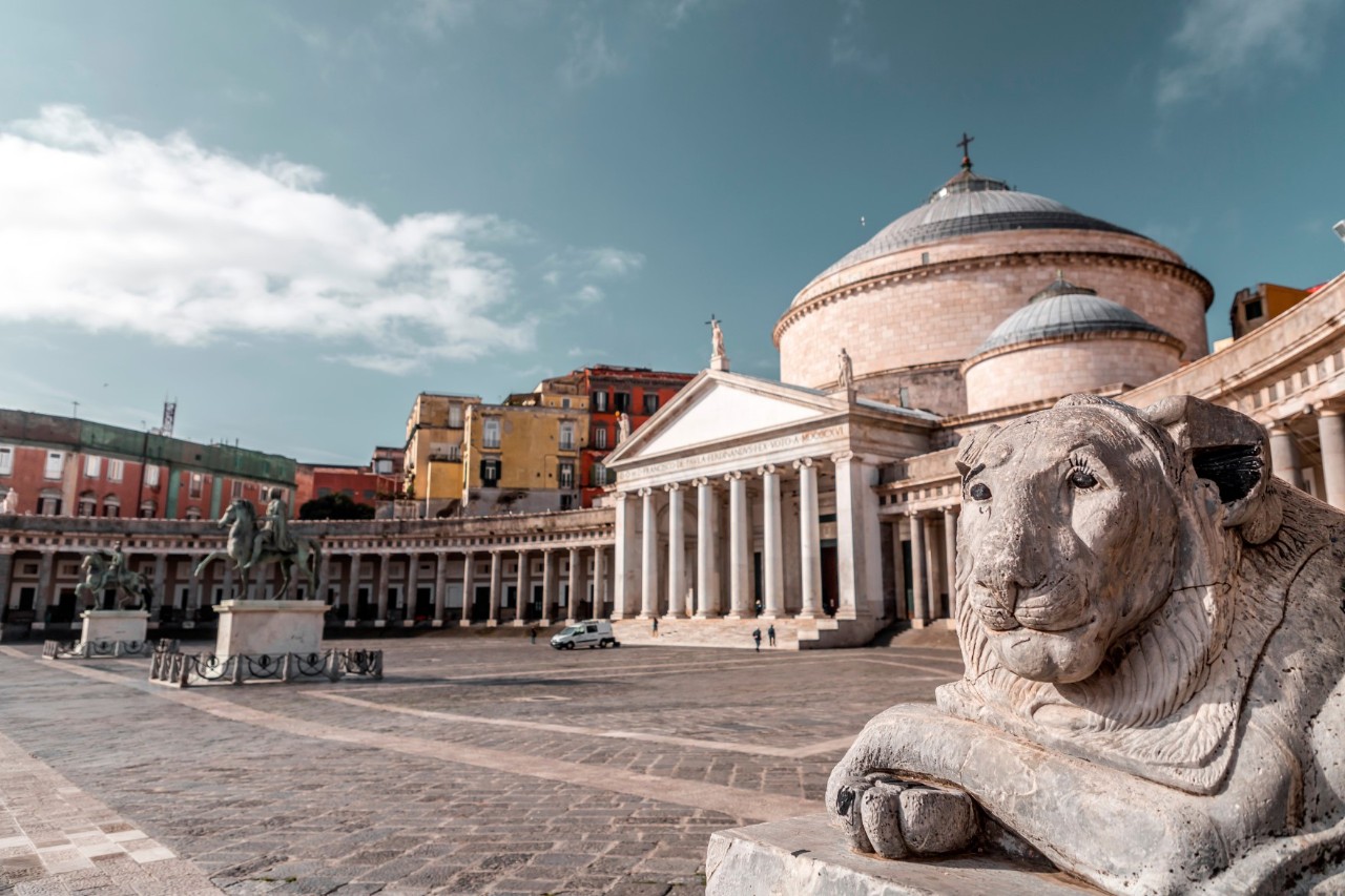 Quiet square with church in the background, tympanum and pillared arch in front. On the right is a stone lion’s head on a pedestal.© EnginKorkmaz/stock.adobe.com