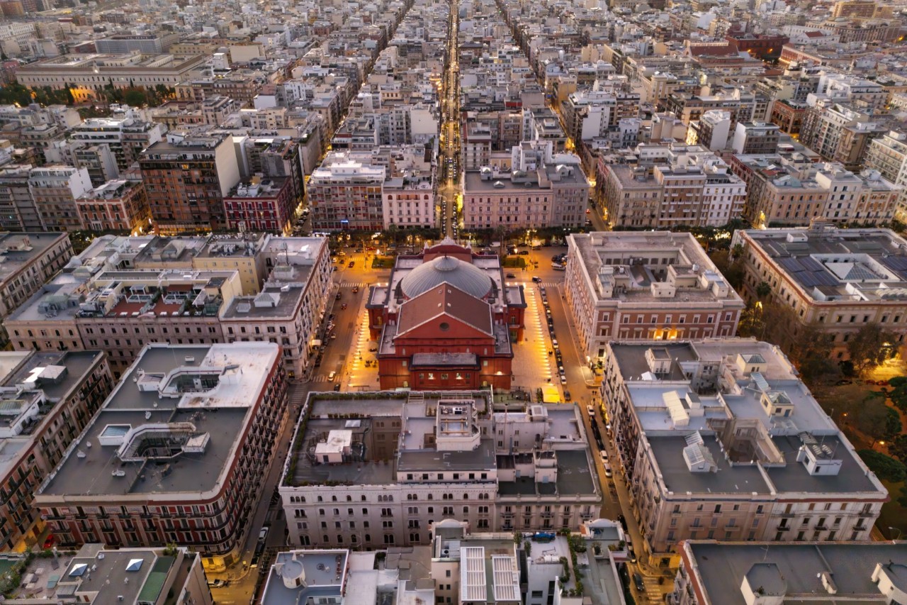 View of a city with straight streets from above. In the centre stands a brightly lit, red domed building. 