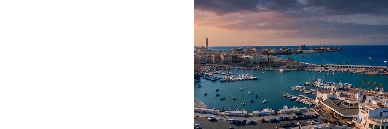 Harbour at dusk. Several boats lie on the dark turquoise water, while the city is bathed in warm light.