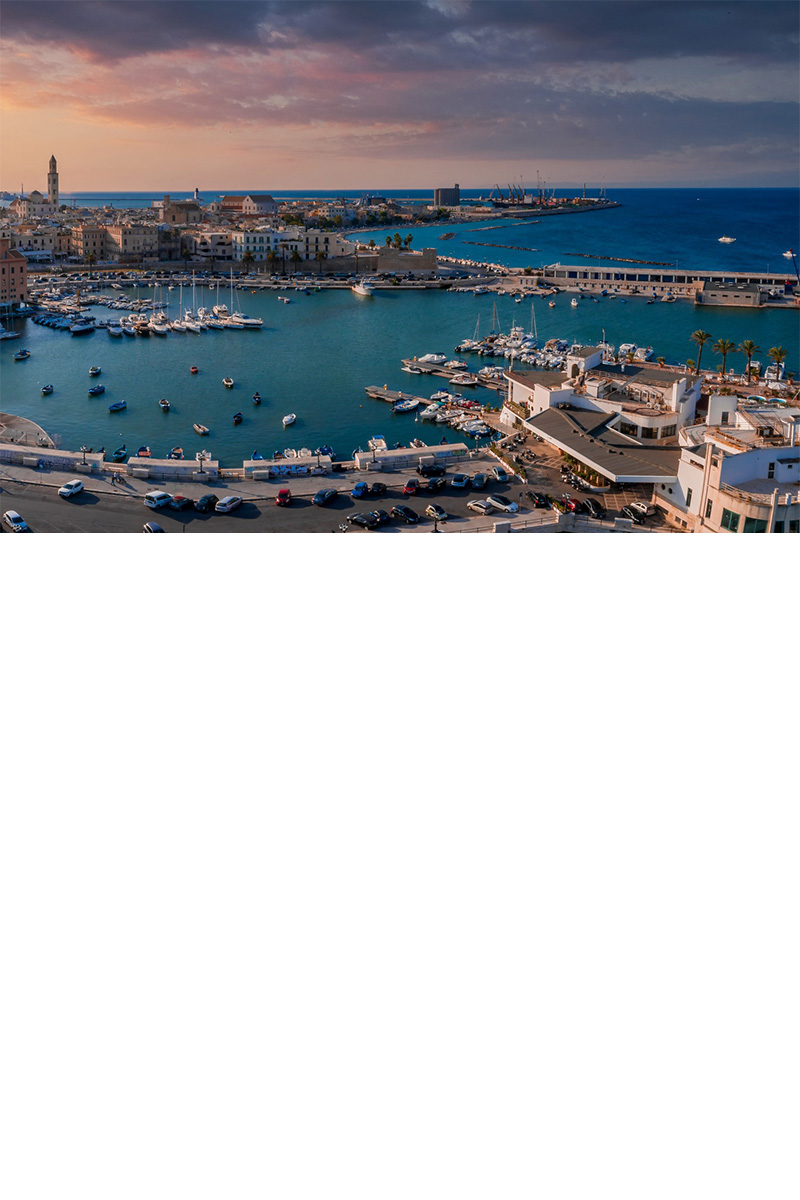 Harbour at dusk. Several boats lie on the dark turquoise water, while the city is bathed in warm light.