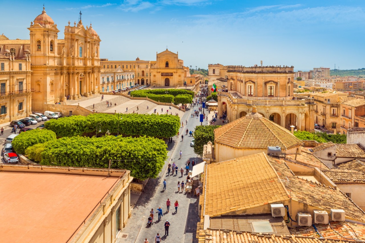 The city of Noto with its magnificent honey-coloured, sandstone buildings, people on the street and green spaces 