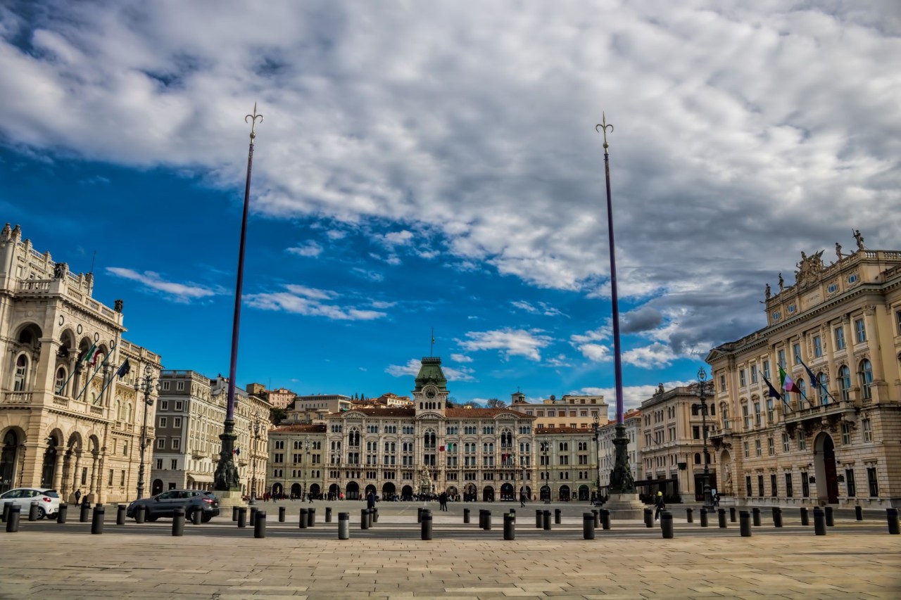 Large square surrounded by magnificent buildings, flagpoles and a blue sky with clouds.