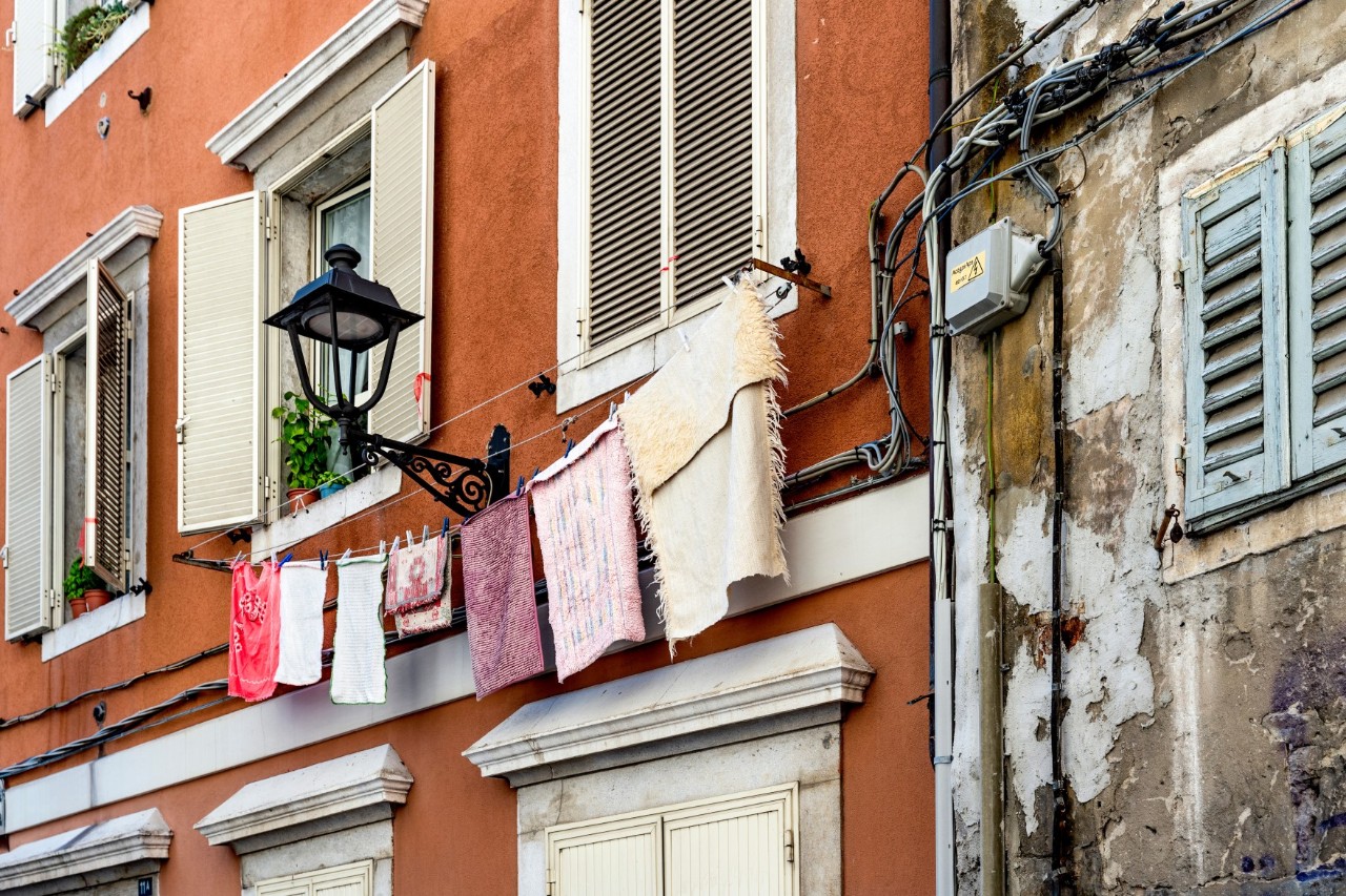 Close-up shot of a red-walled building with towels on a washing line. Next to it stands an old, damaged building. 