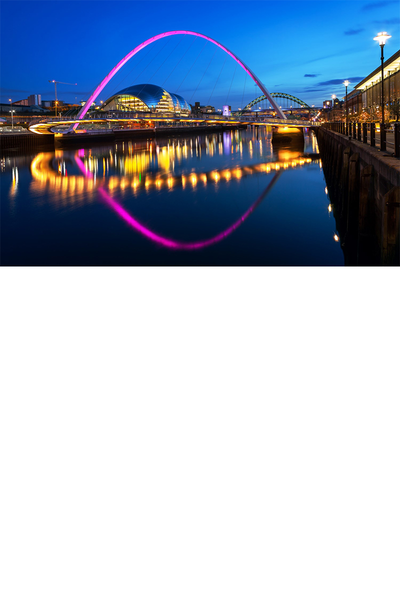 Evening shot of a river in a city, with a pink-lit arched bridge in the foreground, reflected in the water. More lights from the adjacent buildings are reflected in the water. A modern building is visible in the bridge arch, with an additional arched bridge in the background. On the right, in the foreground, there is another illuminated building right on the edge of the riverbank.