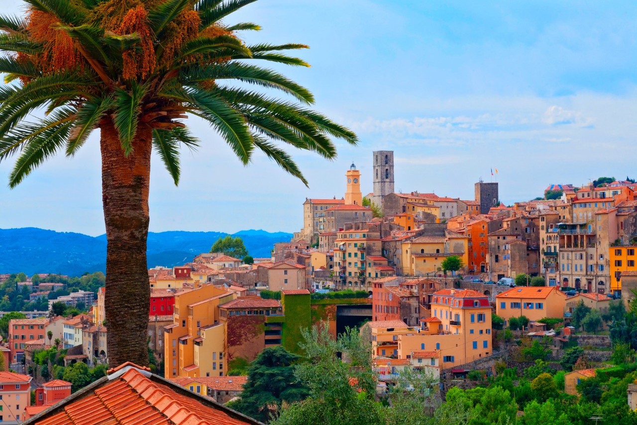 The hilly town of Grasse with colourful houses and church towers, palm tree in the left foreground 