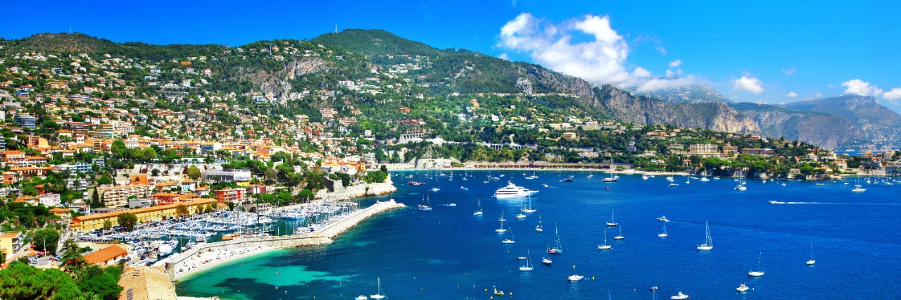 Panoramic view of Nice, populated green hills, harbour and beach, blue ocean with lots of small sailboats © Freesurf/stock.adobe.com