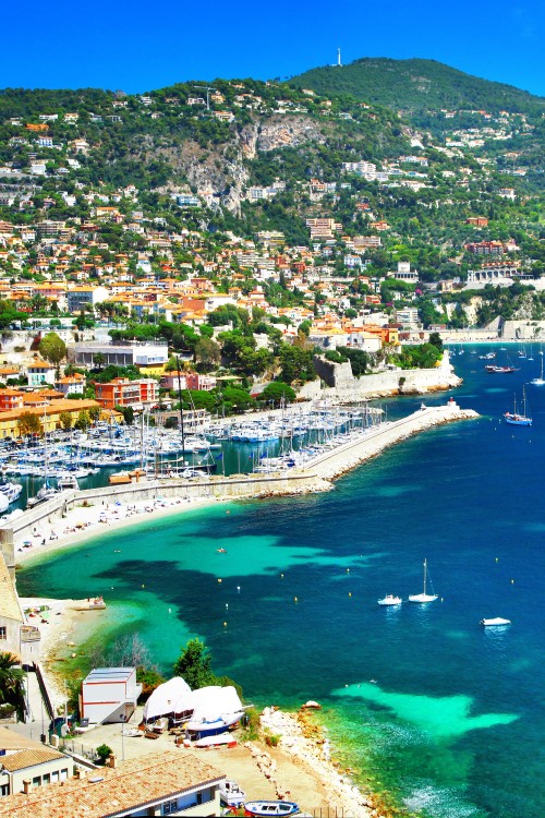 Panoramic view of Nice, populated green hills, harbour and beach, blue ocean with lots of small sailboats © Freesurf/stock.adobe.com
