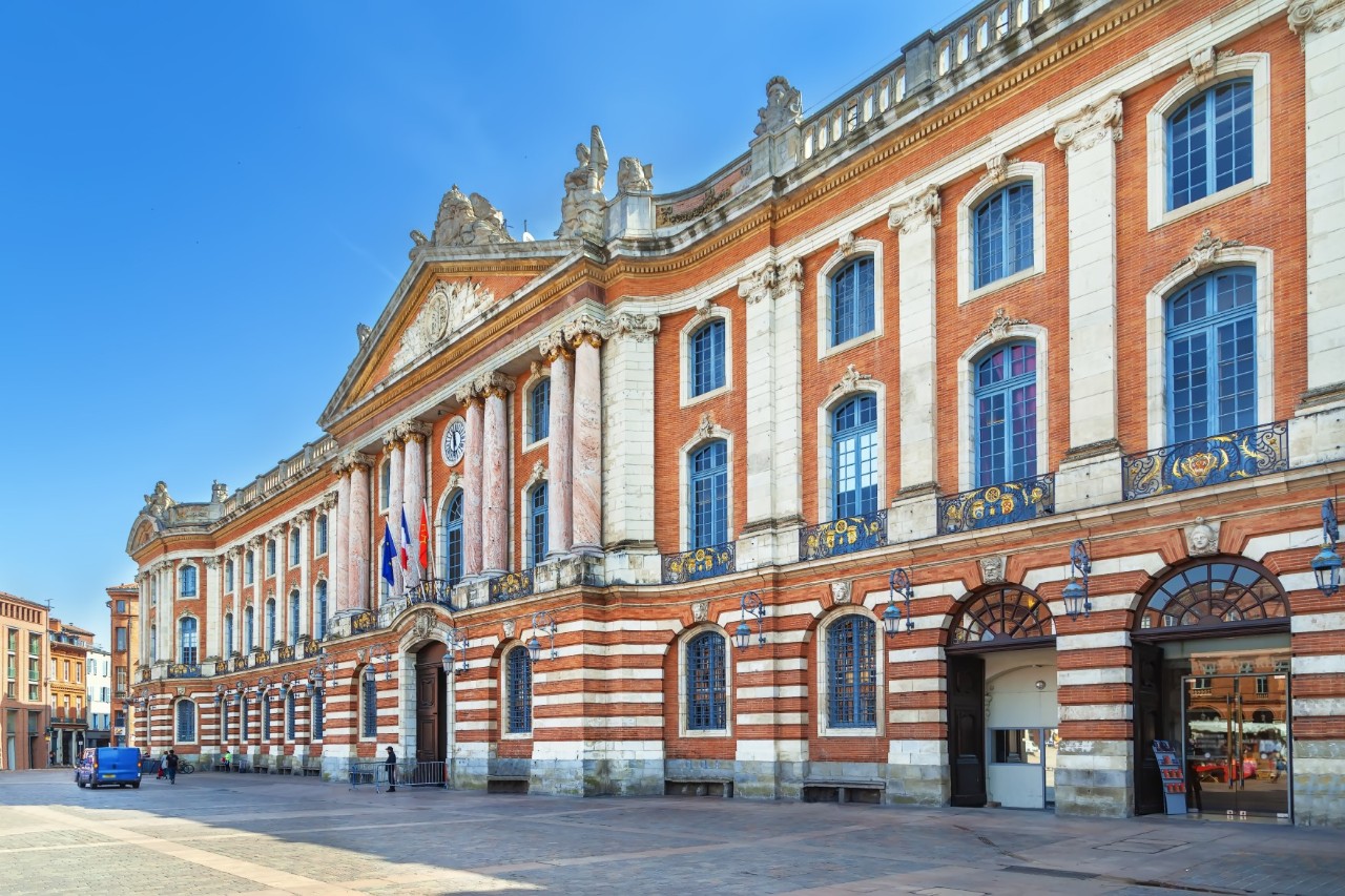 A striking red-and-white building with high windows. A blue vehicle is parked in front of the left end of the building.