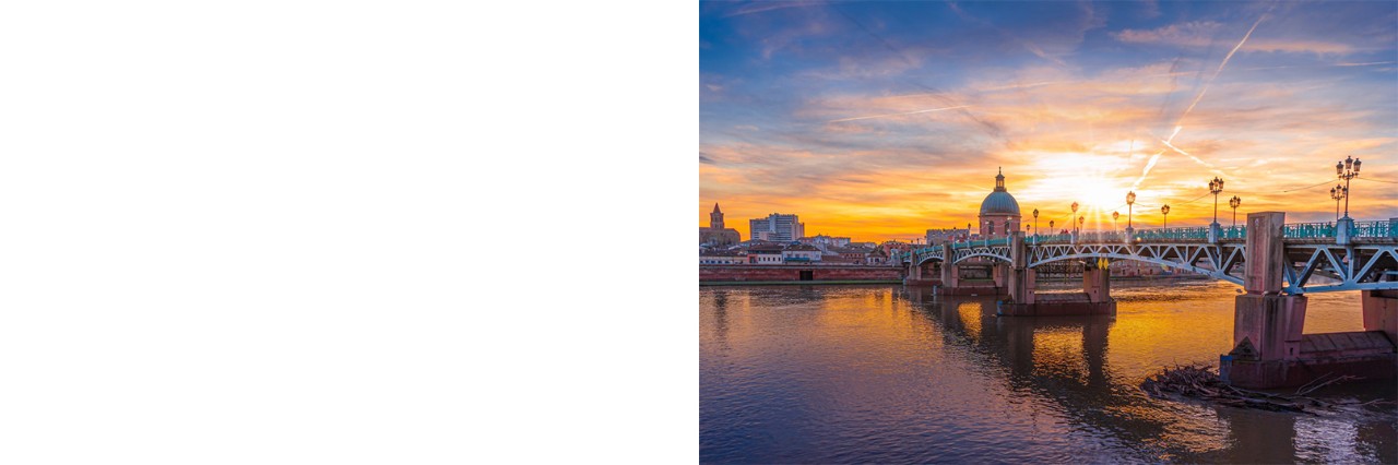 Sunset with a view of a large bridge with lanterns crossing a river. A few buildings as a church dome can be seen on the other side of the river.
