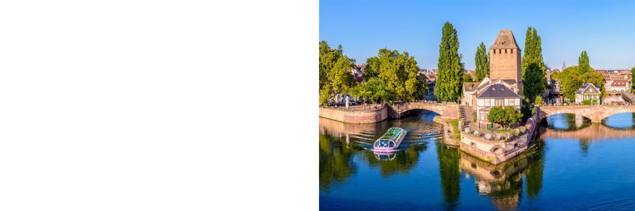 The picture shows a river landscape with three striking defence towers, two boats on the river, old bridges and historic buildings.