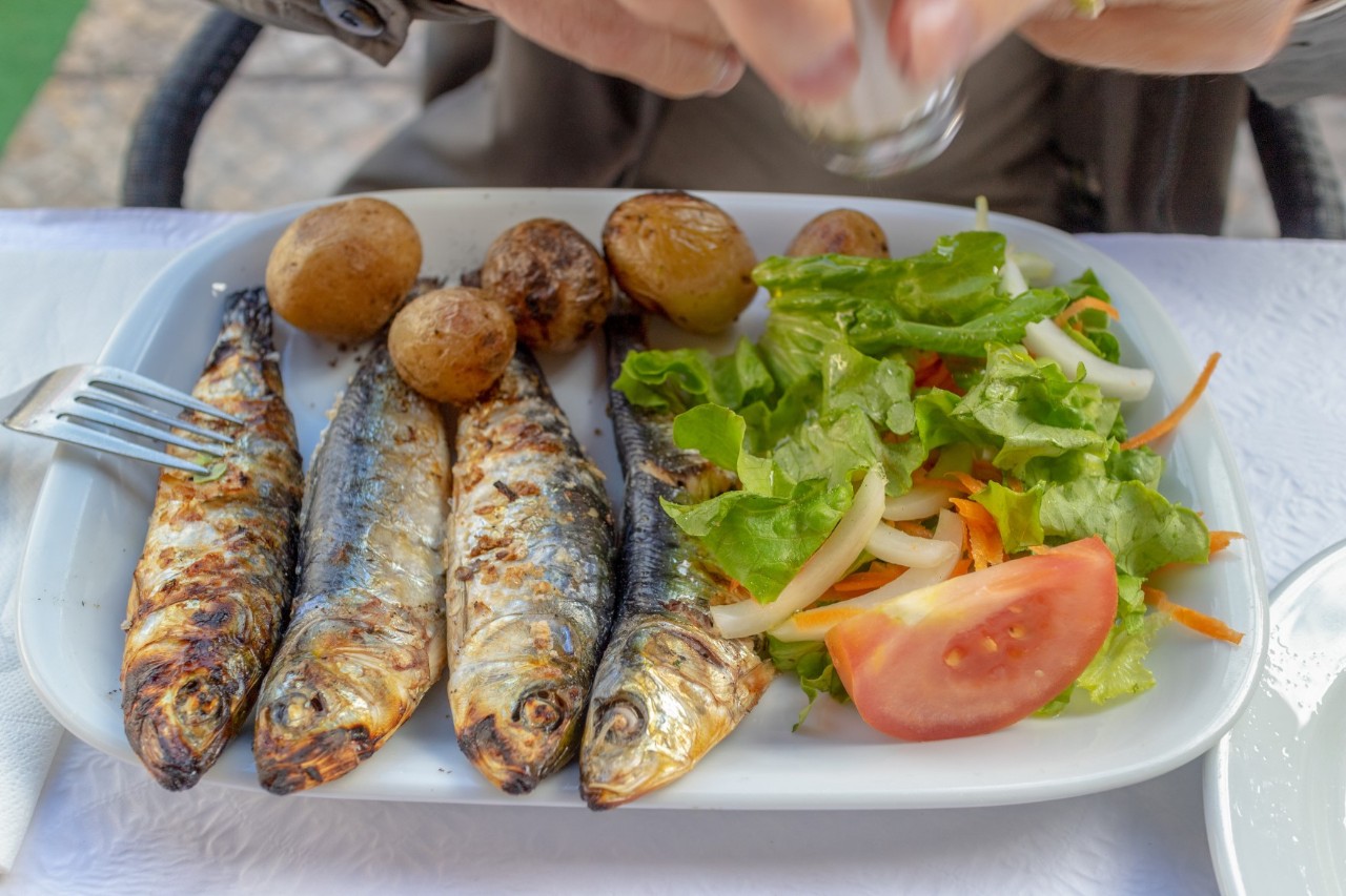 A plate of grilled sardines, potatoes and salad