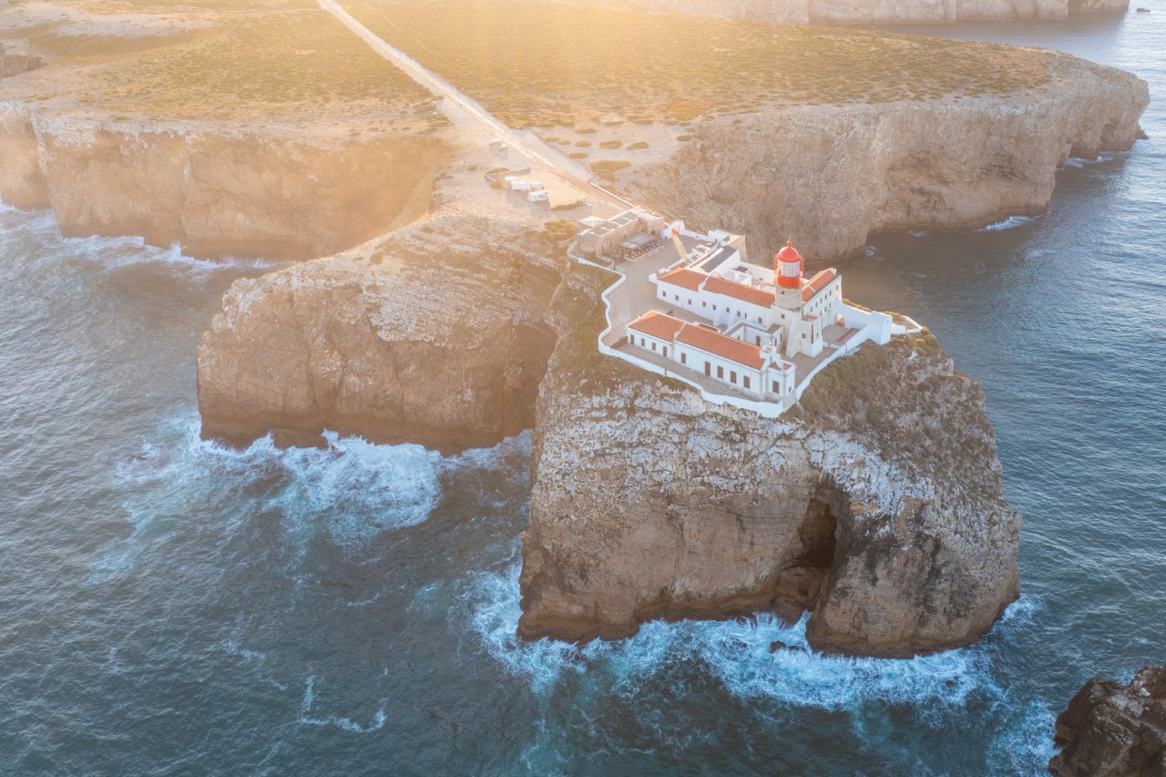 Lighthouse with red roofs on the cliffs of Cabo de São Vicente, rushing sea, rock formations. 