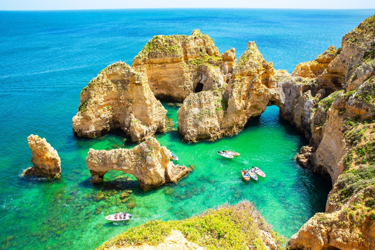 Rock formations in the water on the coast of Ponta da Piedade, turquoise blue water, small boats in the sea, sparsely vegetated cliffs. © Traveller70/stock.adobe.com