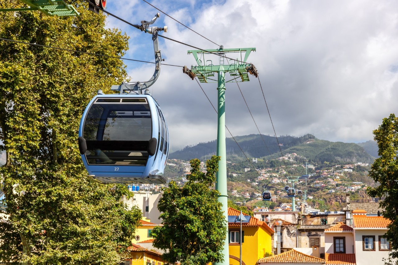 The cable car gondola in the foreground, in the background the sea of buildings with trees and forested mountains in between 