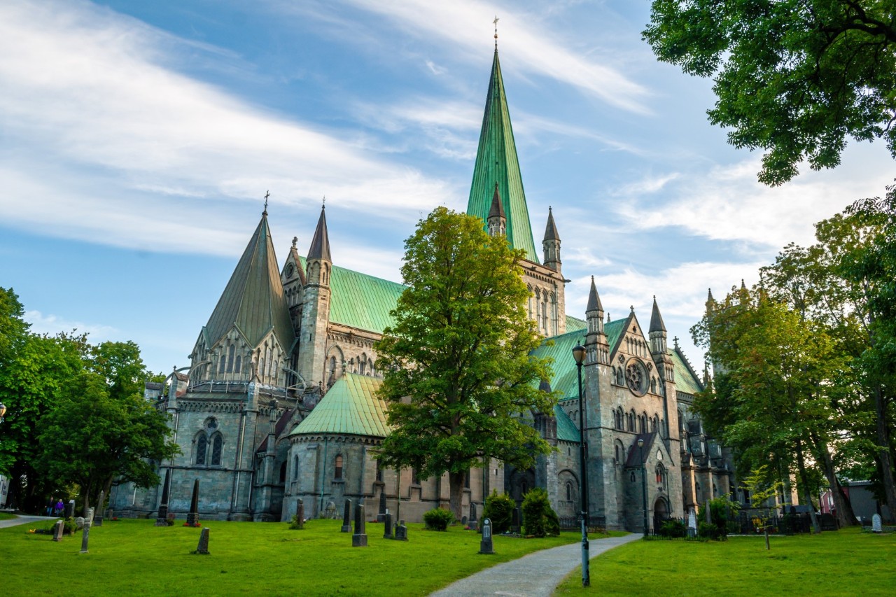 Cathedral with green spire surrounded by a green area and trees. 