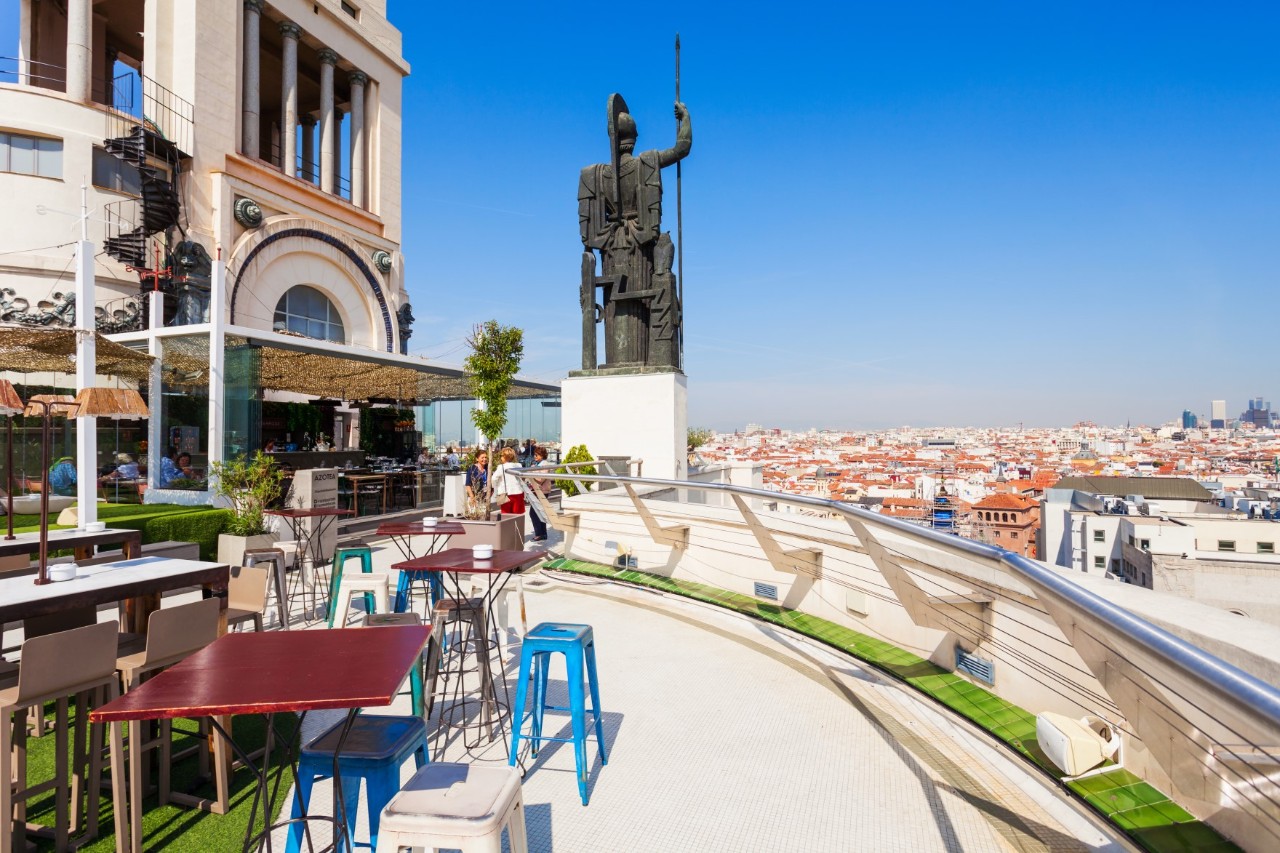 Rooftop bar with statue and city panorama.