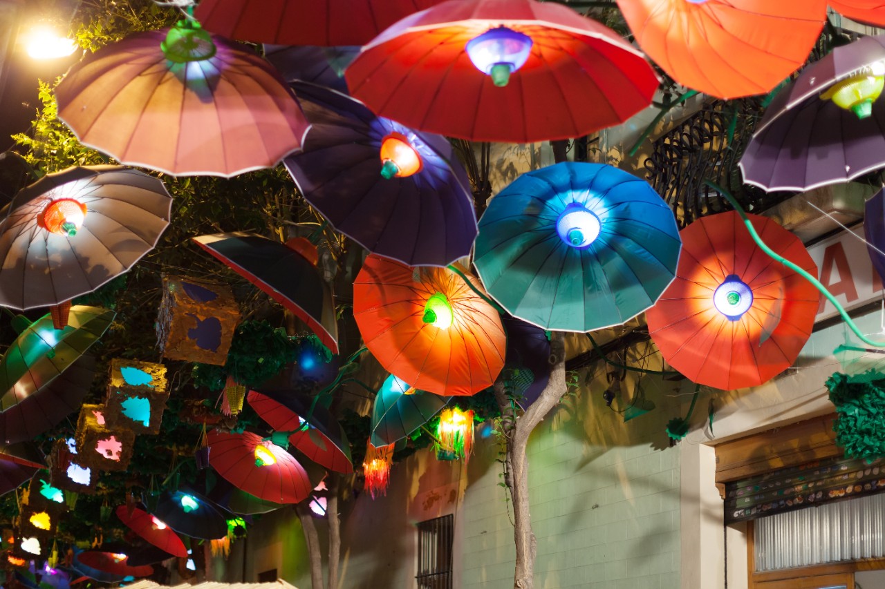 Colorful umbrellas provide shade in a street in the Gràcia district.