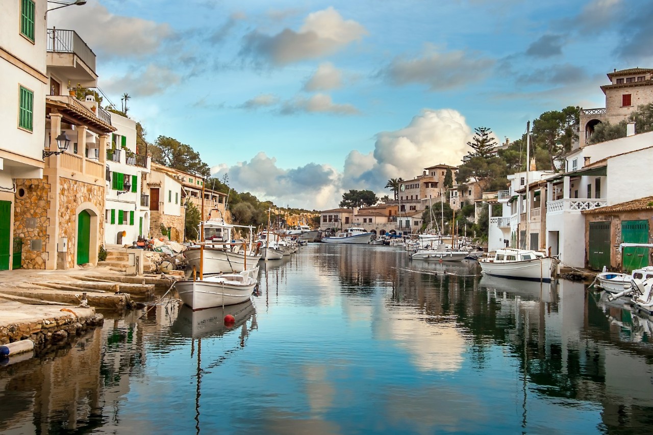 Small canal with pretty houses on both sides and several small boats moored in front 