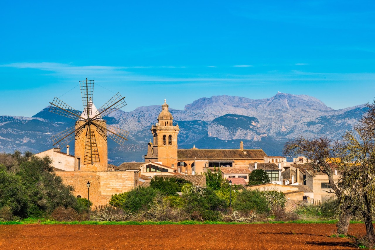 A mountain village with an old windmill and a church in the foreground, mountains can be seen in the background 