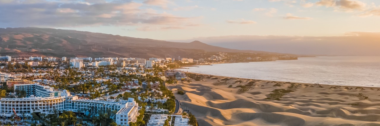 Dune landscape next to hotel. Behind it, mountains and sea at sunrise.