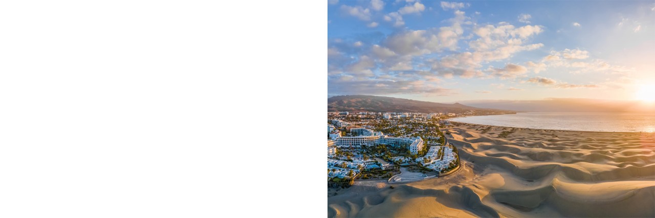 Dune landscape by hotel, with mountains and sea in the sunrise behind.