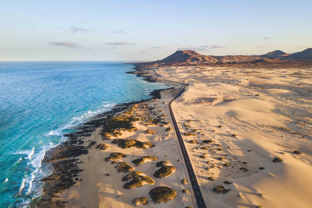 Dunes by the sea with coastal road and view of the blue water.